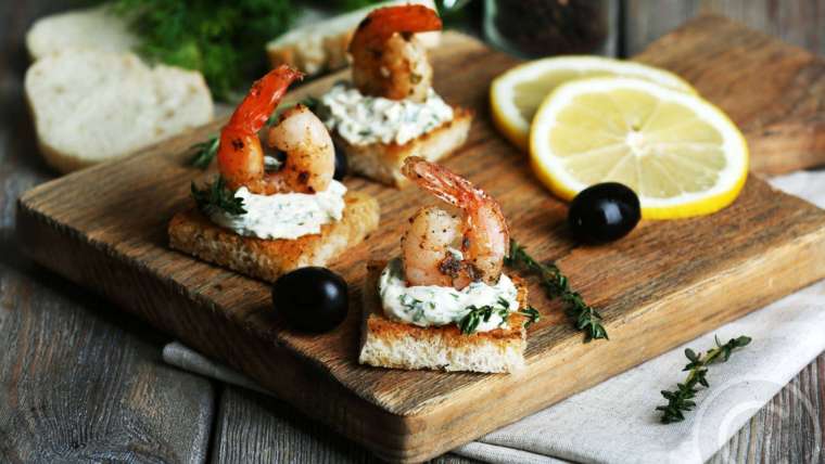 A wooden board with some shrimp and olives on it