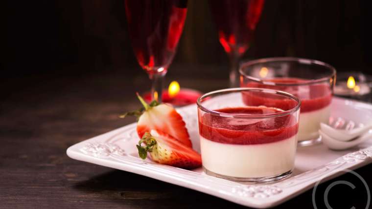 A white plate topped with strawberry cheesecake next to two glasses.