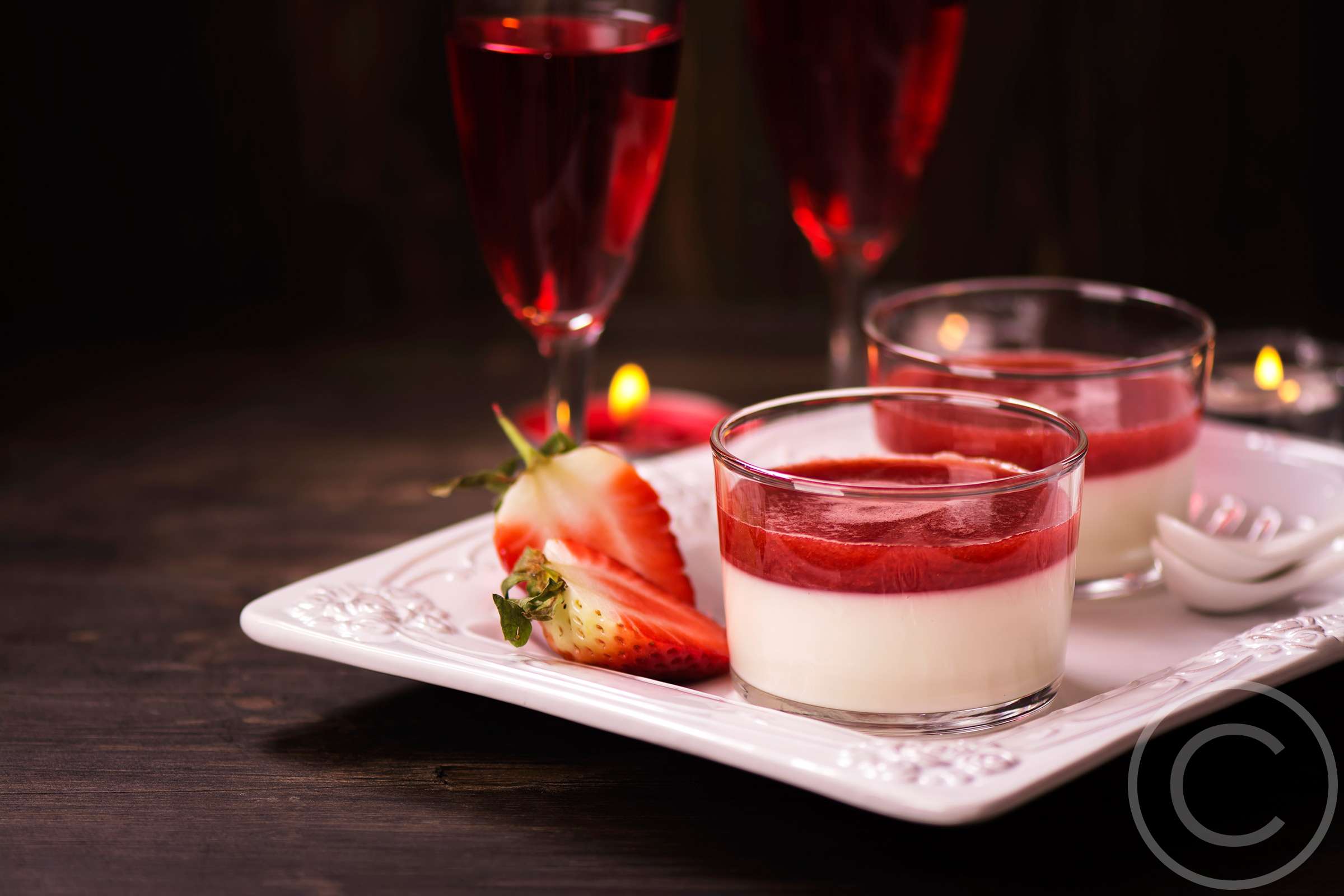 A white plate topped with strawberry cheesecake next to two glasses.